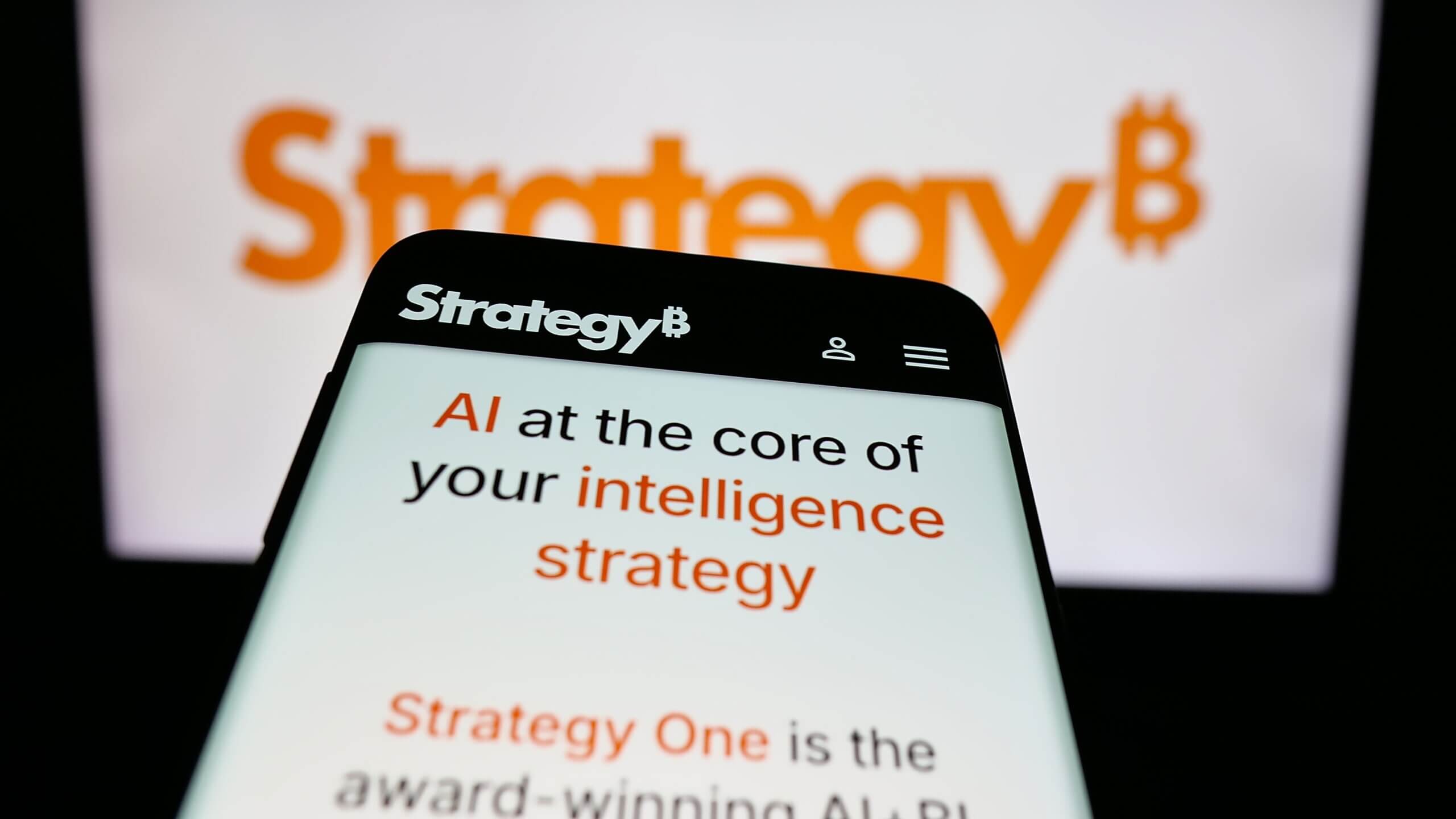 Layar ponsel cerdas menampilkan situs web StrategyB dengan teks tentang AI dan strategi intelijen, logo StrategyB kabur di latar belakang.