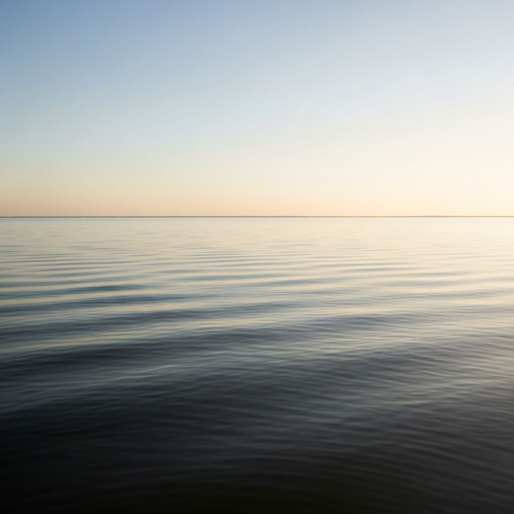 Air laut yang tenang di bawah langit cerah saat matahari terbit atau terbenam dengan riak lembut di permukaan.