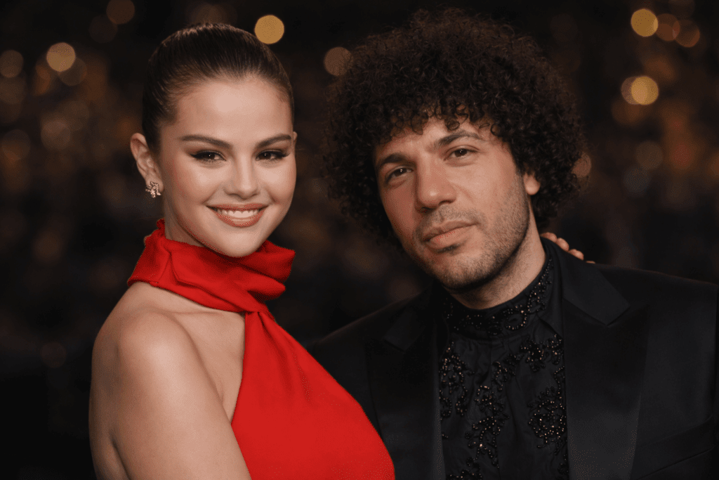 Selena Gomez dalam balutan gaun merah dan seorang pria berjas hitam berpose bersama di sebuah acara formal.