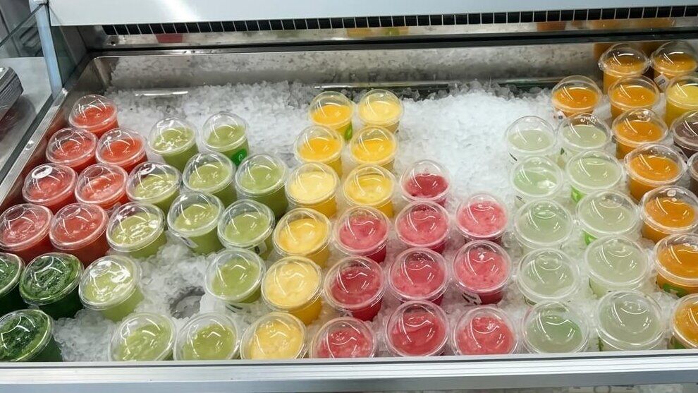 Berbagai macam gambar jus buah dan sayuran berwarna-warni dalam gelas plastik bening di atas es dalam etalase berpendingin