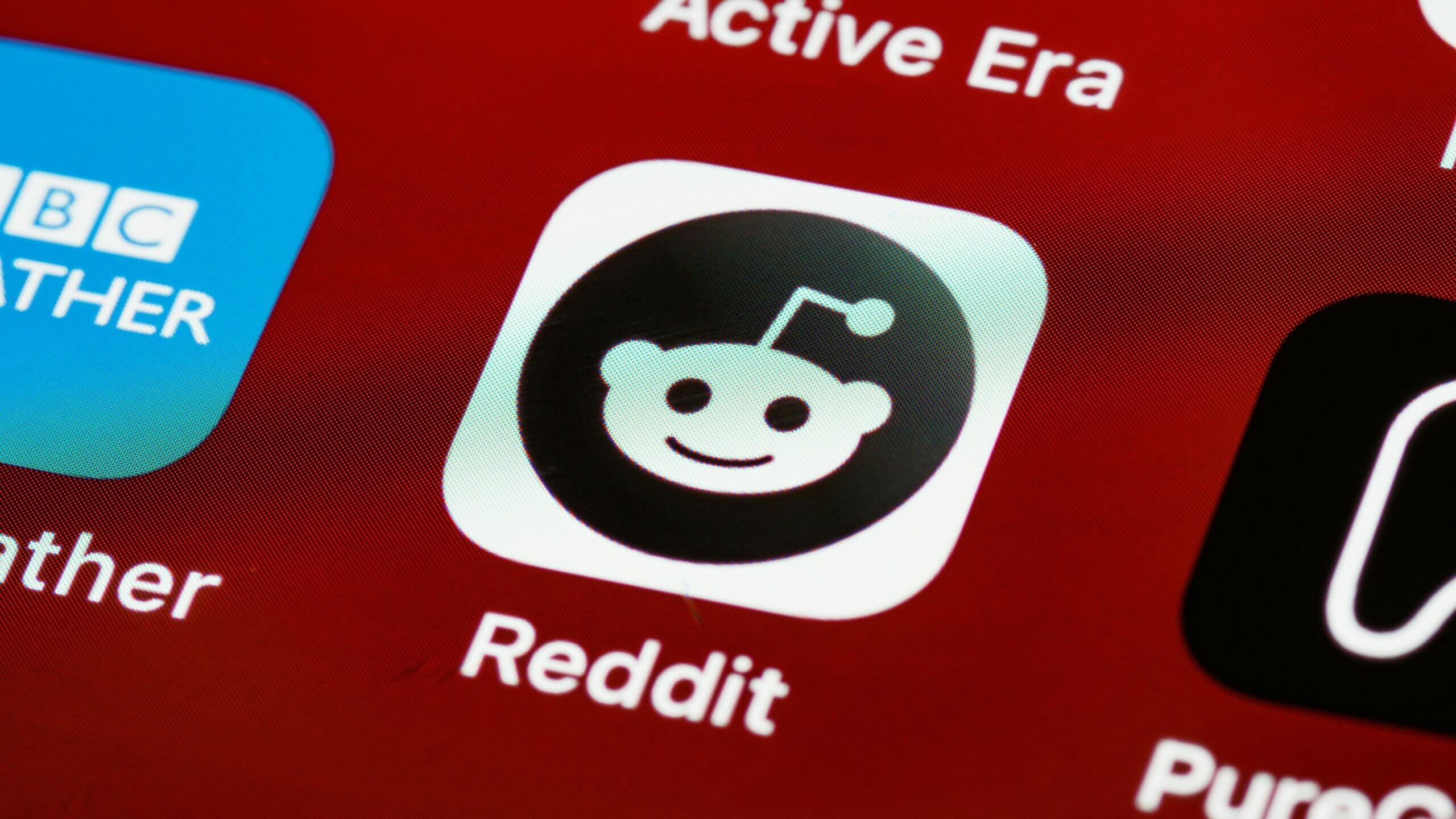 Ikon aplikasi Reddit di layar ponsel pintar dengan latar belakang merah.