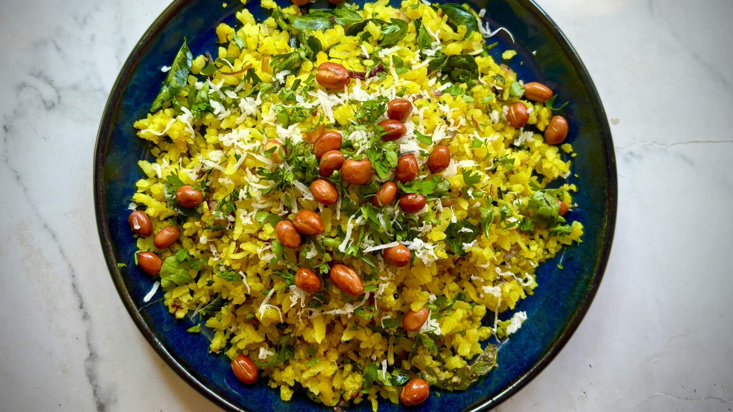 Poha dihias dengan kacang tanah, kelapa parut, dan daun ketumbar segar di piring biru.