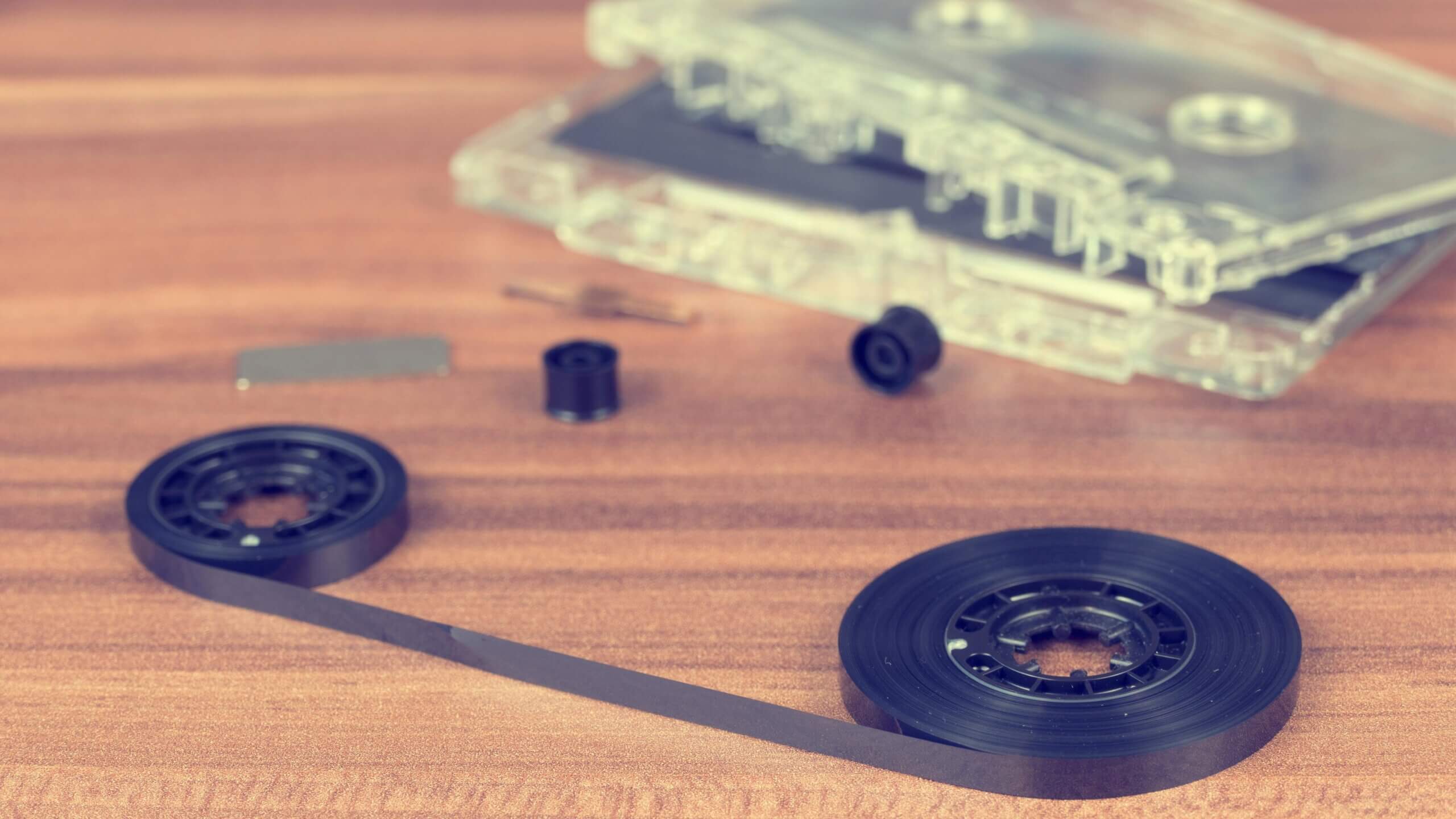 Pita kaset bening yang dibongkar dengan gulungan pita hitam longgar pada permukaan kayu