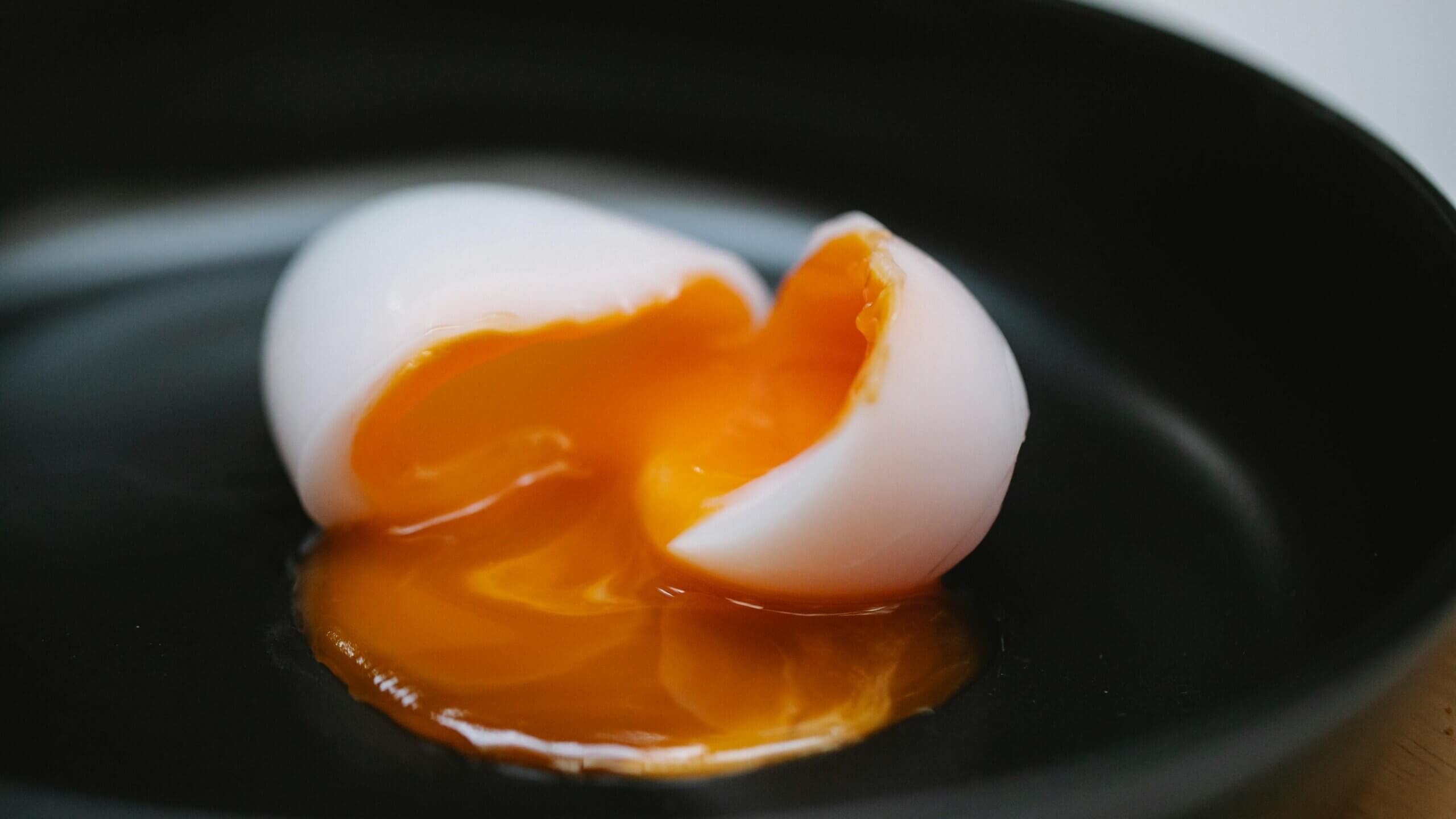 Telur rebus setengah terbuka dengan kuning telur encer di piring hitam