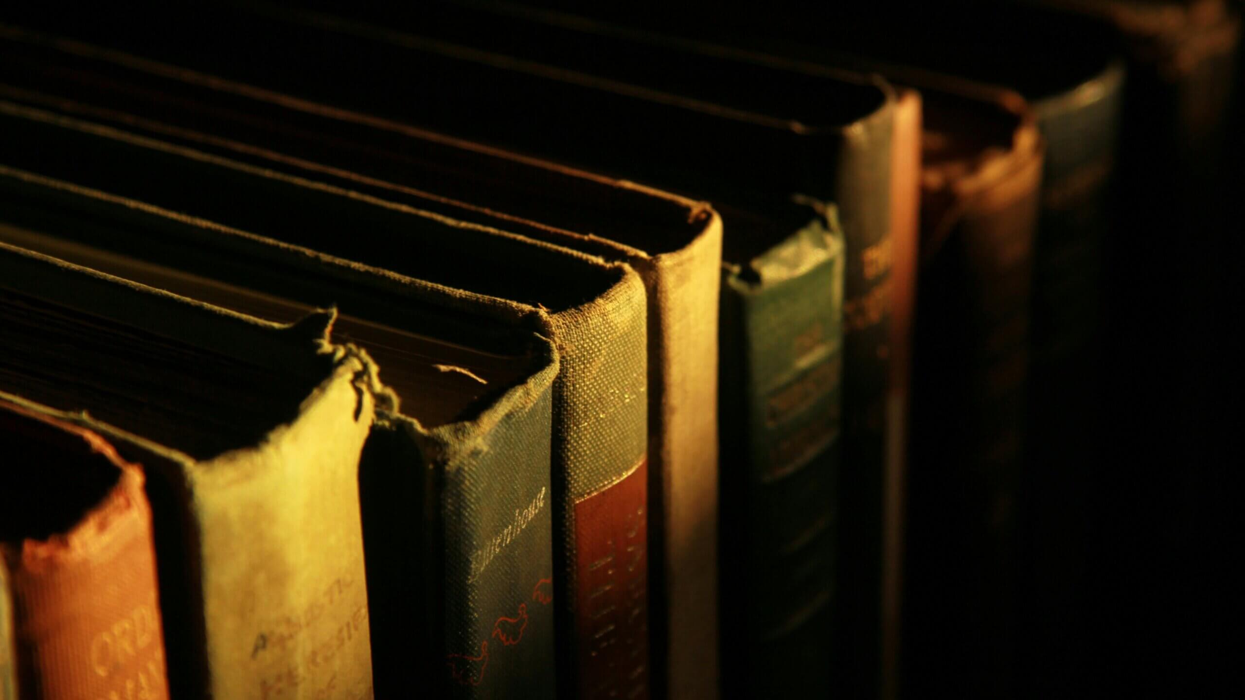 Tampilan jarak dekat dari buku-buku hardcover vintage yang usang di rak yang remang-remang.