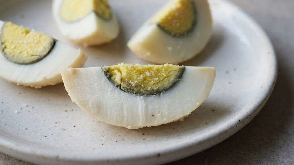Irisan telur abad dengan lapisan luar berwarna putih bening dan kuning telur kehijauan di piring putih