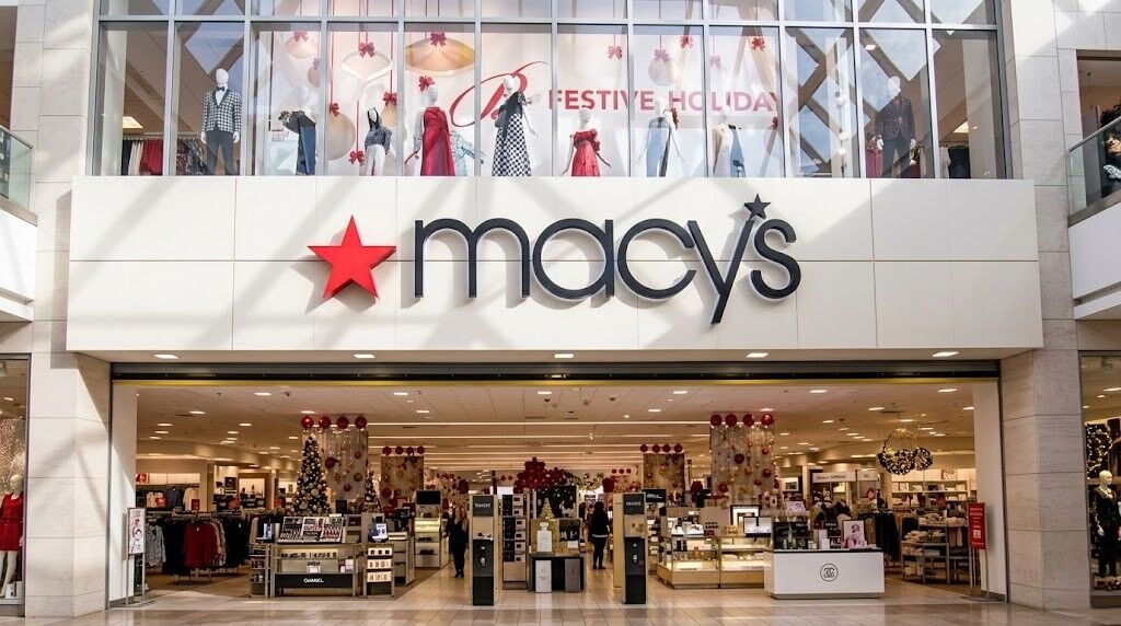 Pintu masuk toko Macy dengan dekorasi hari raya dan manekin yang mengenakan pakaian pesta di atasnya.
