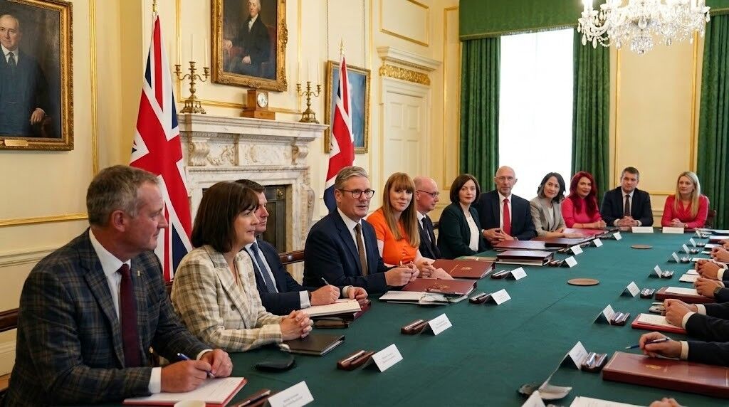Perdana Menteri Inggris Keir Starmer dan para pejabat duduk di meja konferensi dengan bendera Inggris di ruang formal.