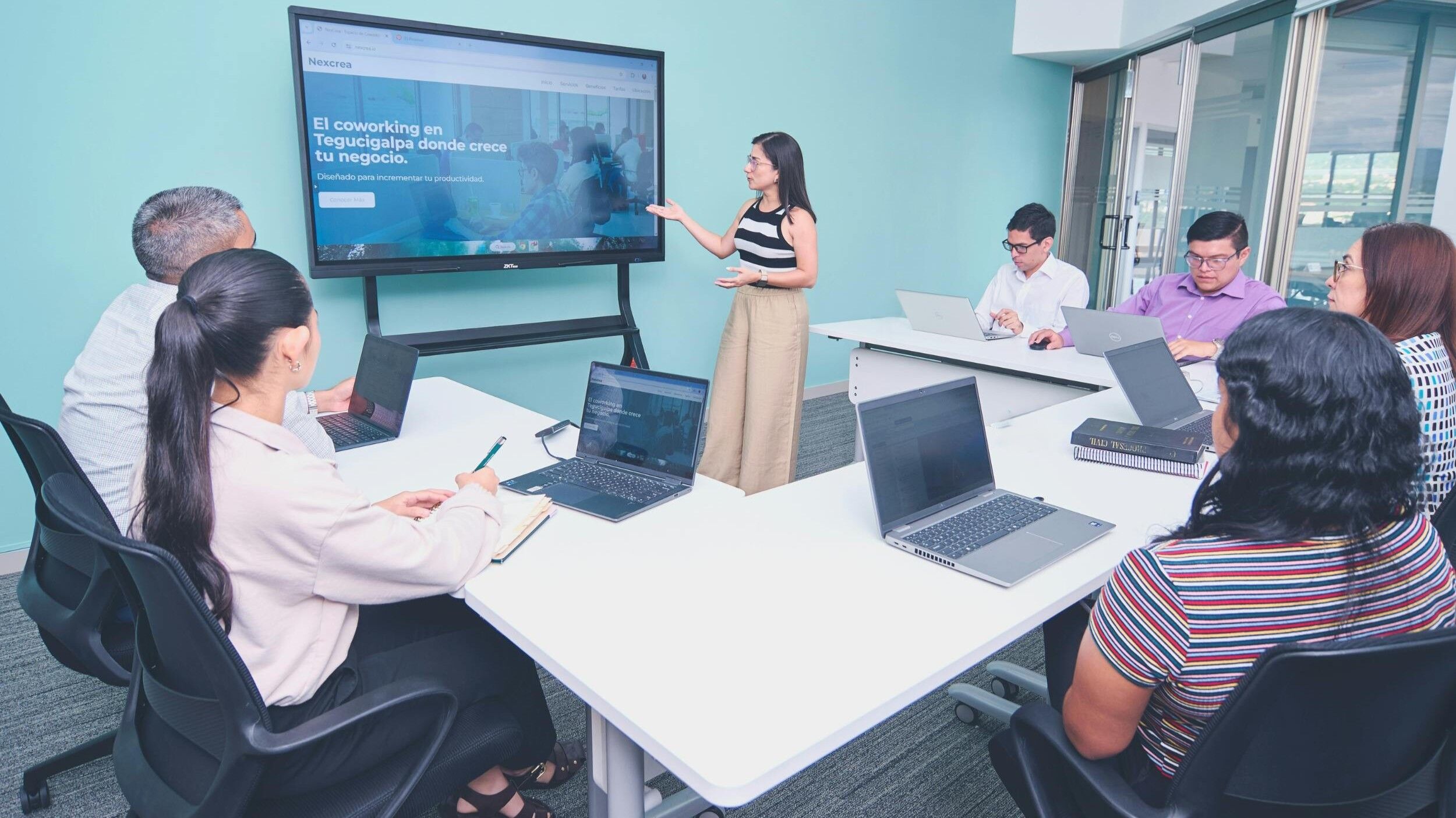 Wanita yang mempresentasikan situs web ruang kerja bersama kepada enam rekannya di ruang rapat kantor modern