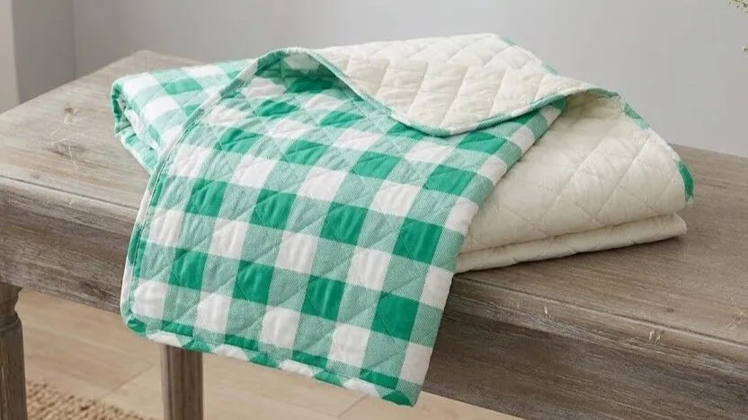 Selimut kotak-kotak hijau dan putih terlipat di atas meja kayu dengan bagian bawah berlapis krem ​​terlihat