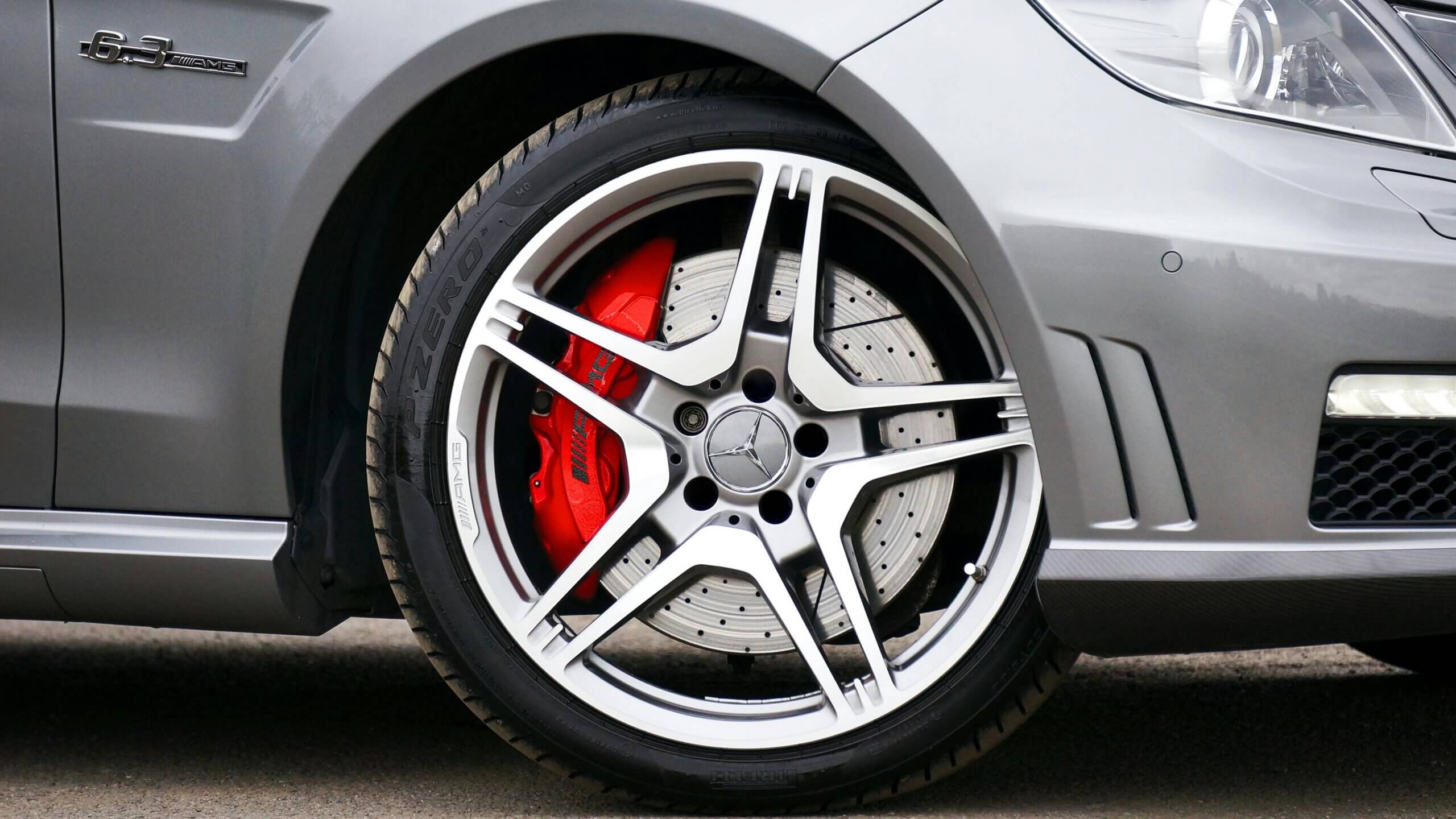 Lencana Mercedes AMG 6.3 dan roda dengan kaliper rem AMG merah di sisi depan mobil berwarna perak