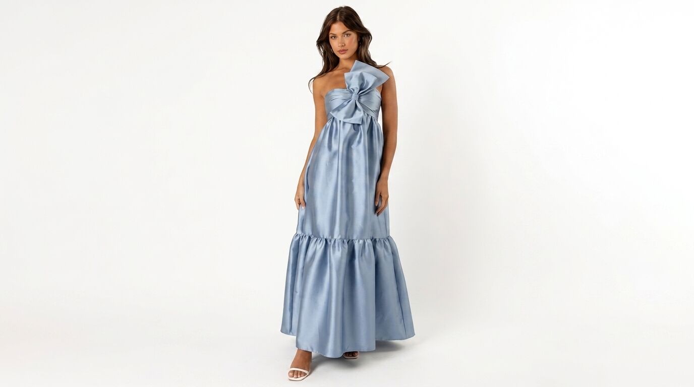 Wanita mengenakan gaun satin biru muda strapless dengan detail pita besar dan pinggiran berkerut, berpose dengan latar belakang putih.