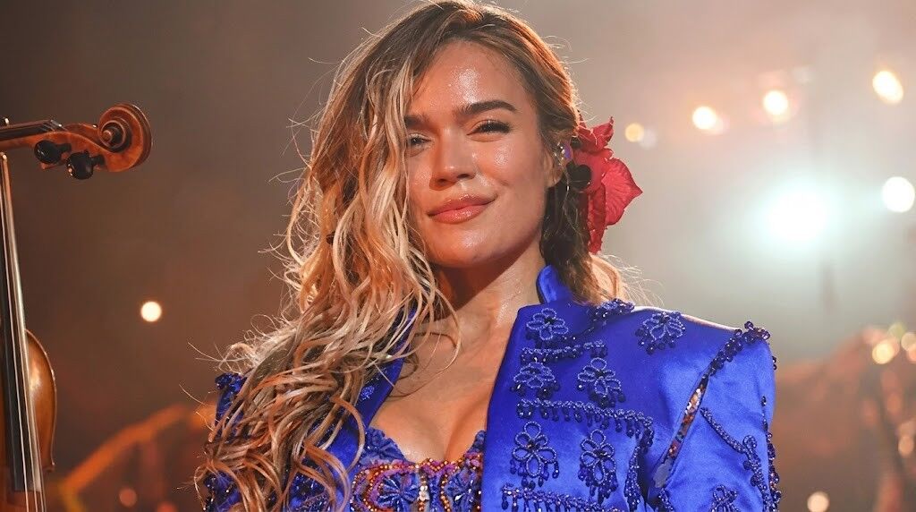 Penyanyi yang mengenakan pakaian berhias biru dengan bunga merah di rambutnya tampil di atas panggung.