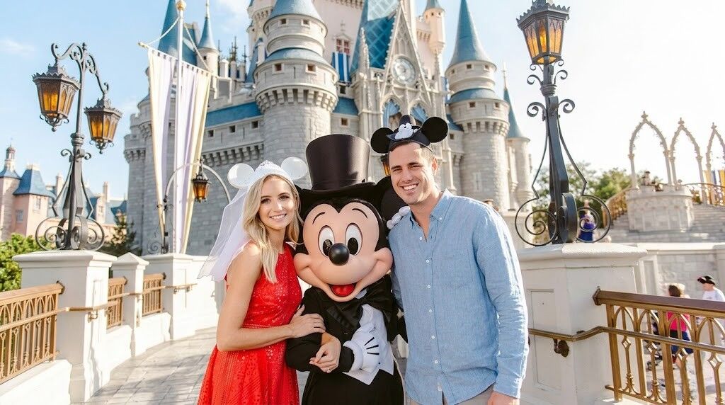 Pasangan yang memakai telinga Mickey berpose dengan Mickey Mouse di depan Kastil Cinderella di Disney World