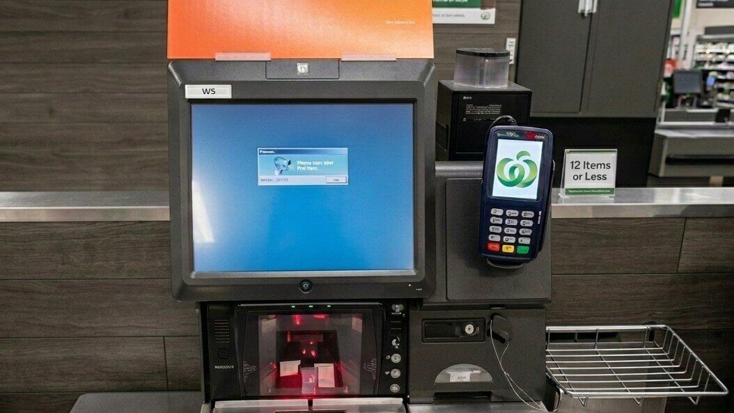 Mesin pembayaran mandiri dengan layar kesalahan biru dan pembaca kartu menampilkan logo Woolworths di toko kelontong.