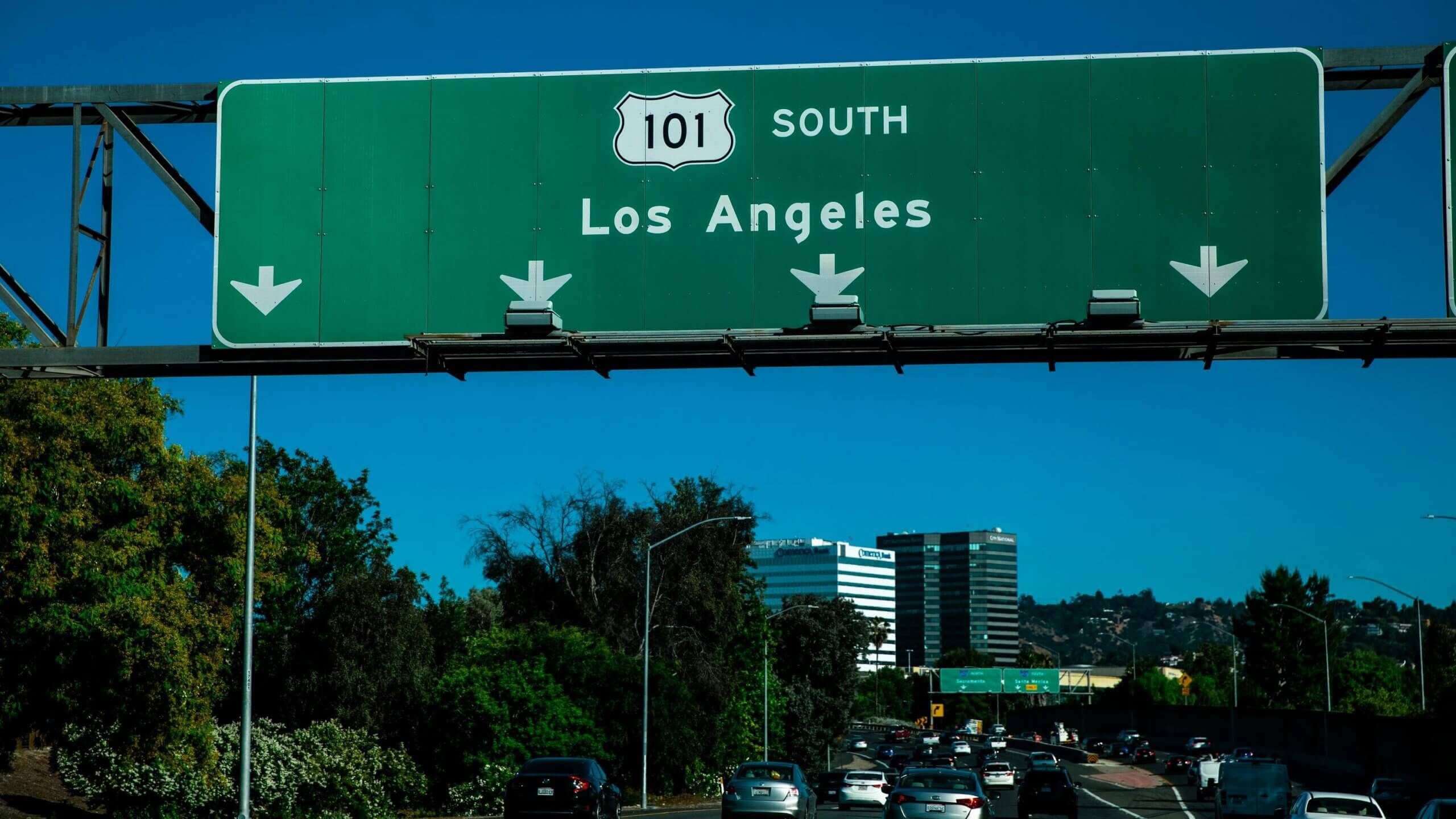 Highway 101 South green road sign untuk Los Angeles di atas lalu lintas jalan bebas hambatan yang sibuk dengan bangunan dan pepohonan di latar belakang