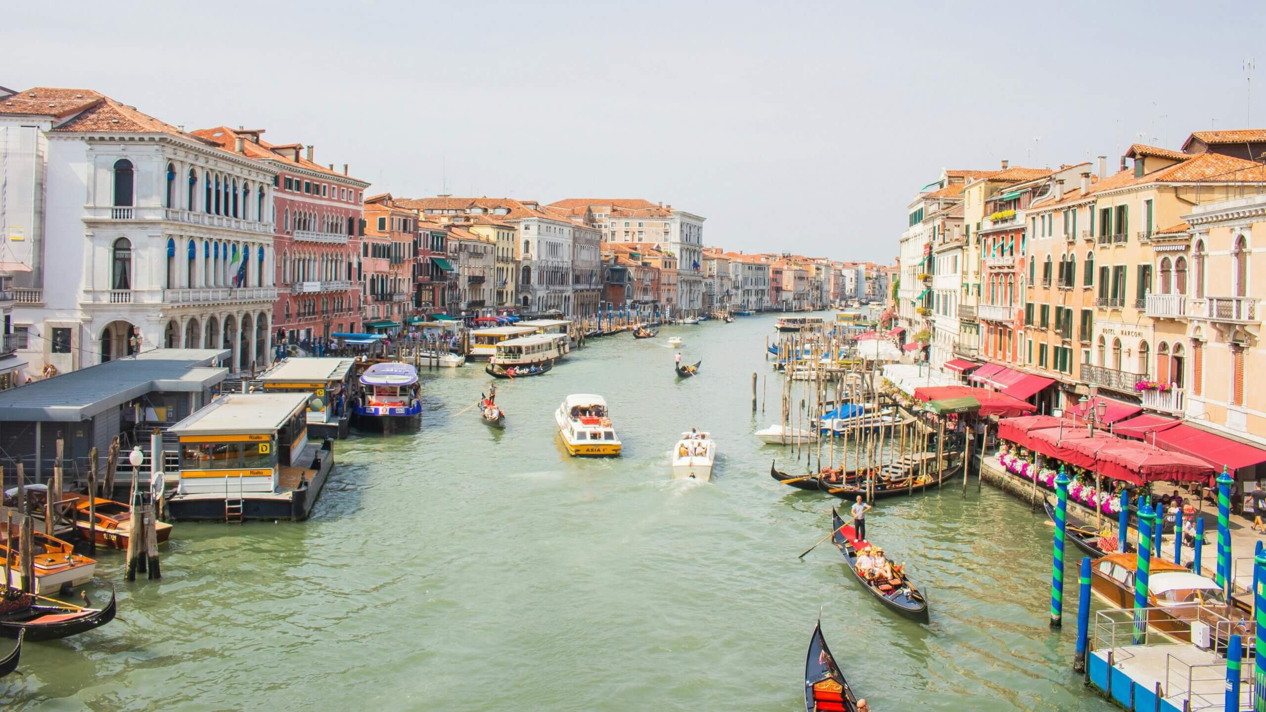 Canal Grande di Venesia dengan gondola, perahu, dan bangunan bersejarah di sepanjang tepi laut di bawah langit cerah