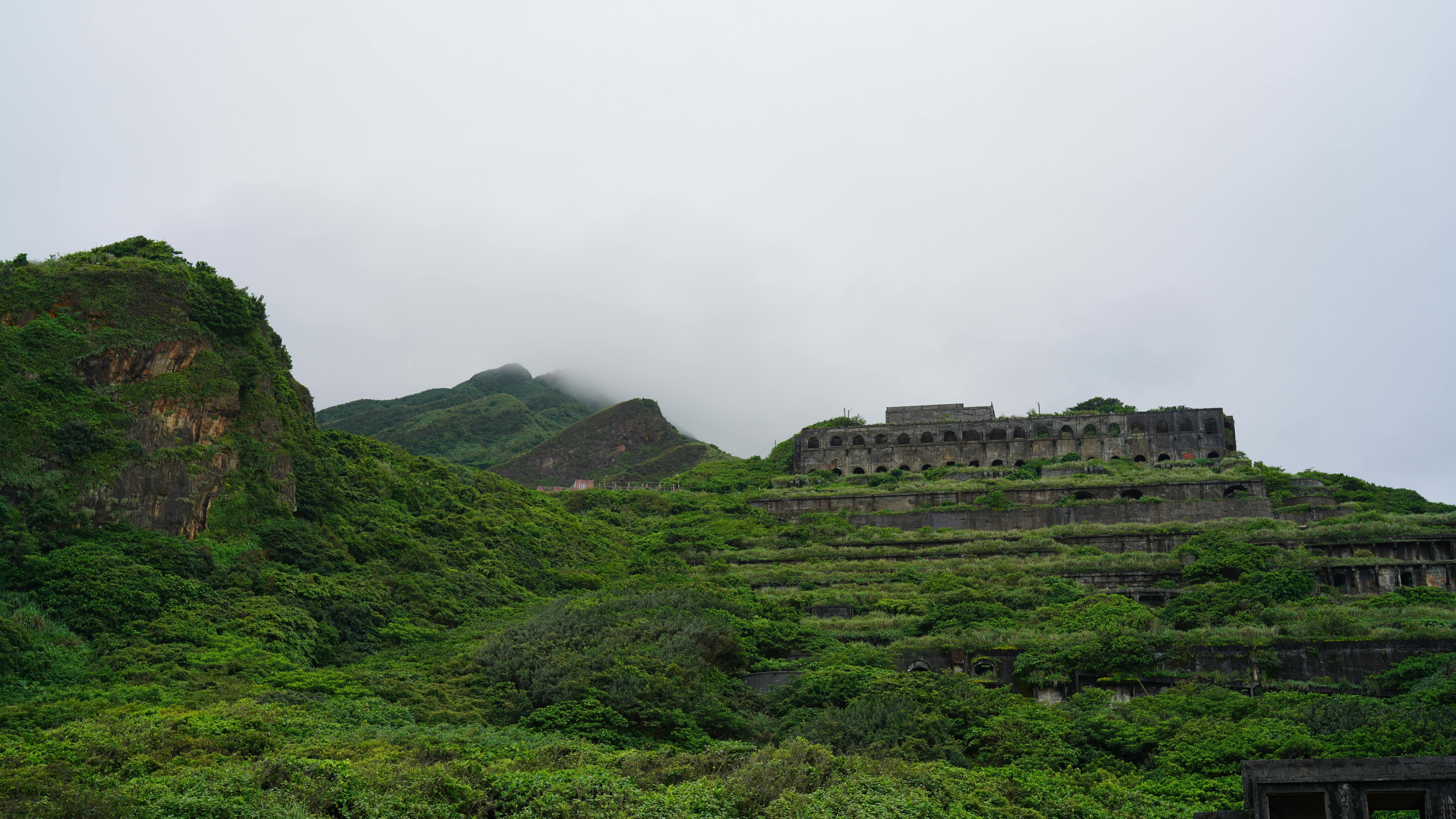 Lereng bukit bertingkat yang ditumbuhi dengan struktur beton besar yang ditinggalkan di bawah langit mendung.
