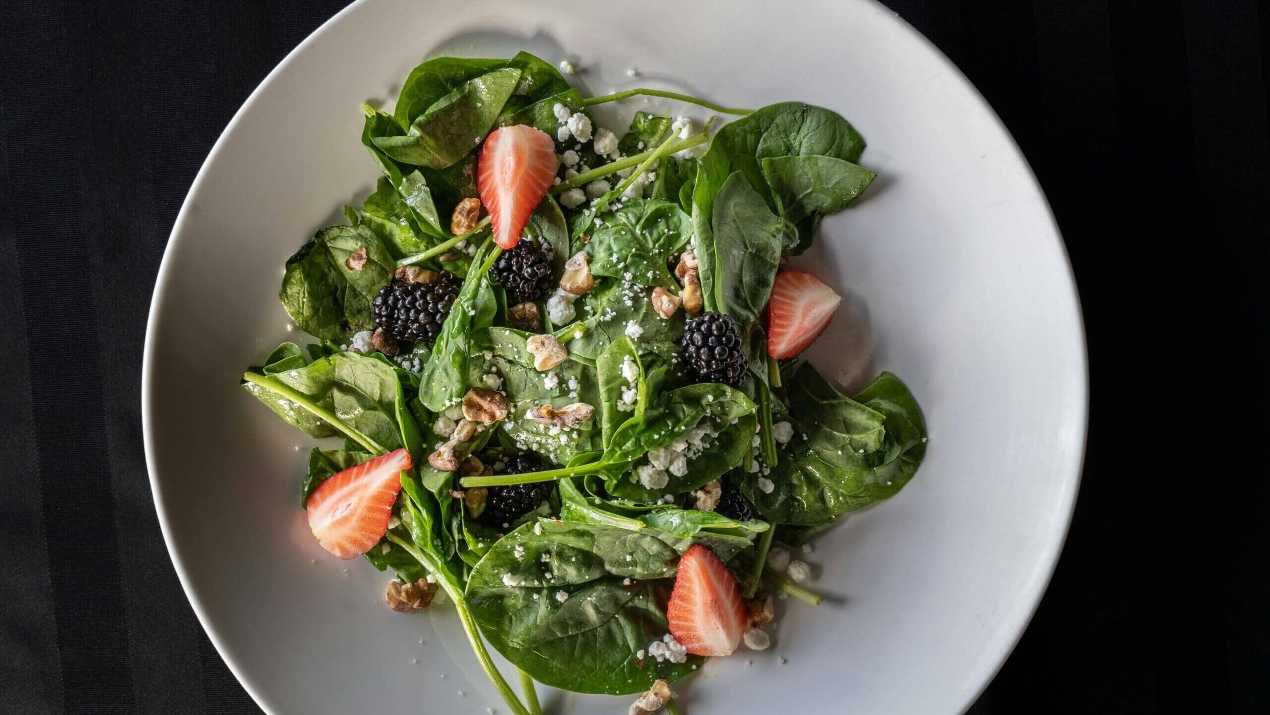 Salad bayam dengan stroberi, blackberry, kenari, dan keju hancur di piring putih