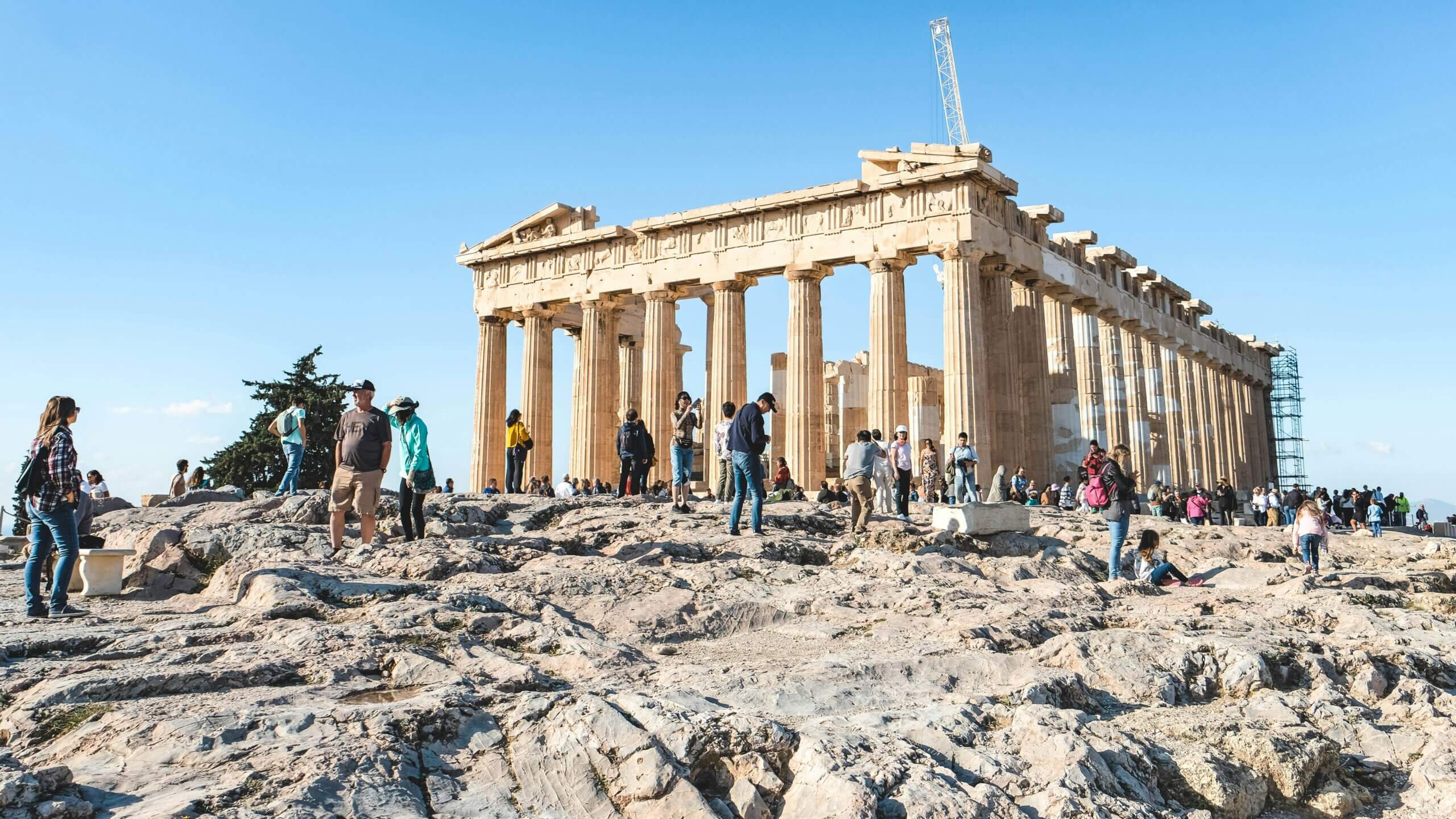 Wisatawan menjelajahi reruntuhan kuil Parthenon pada hari yang cerah di Athena, Yunani.