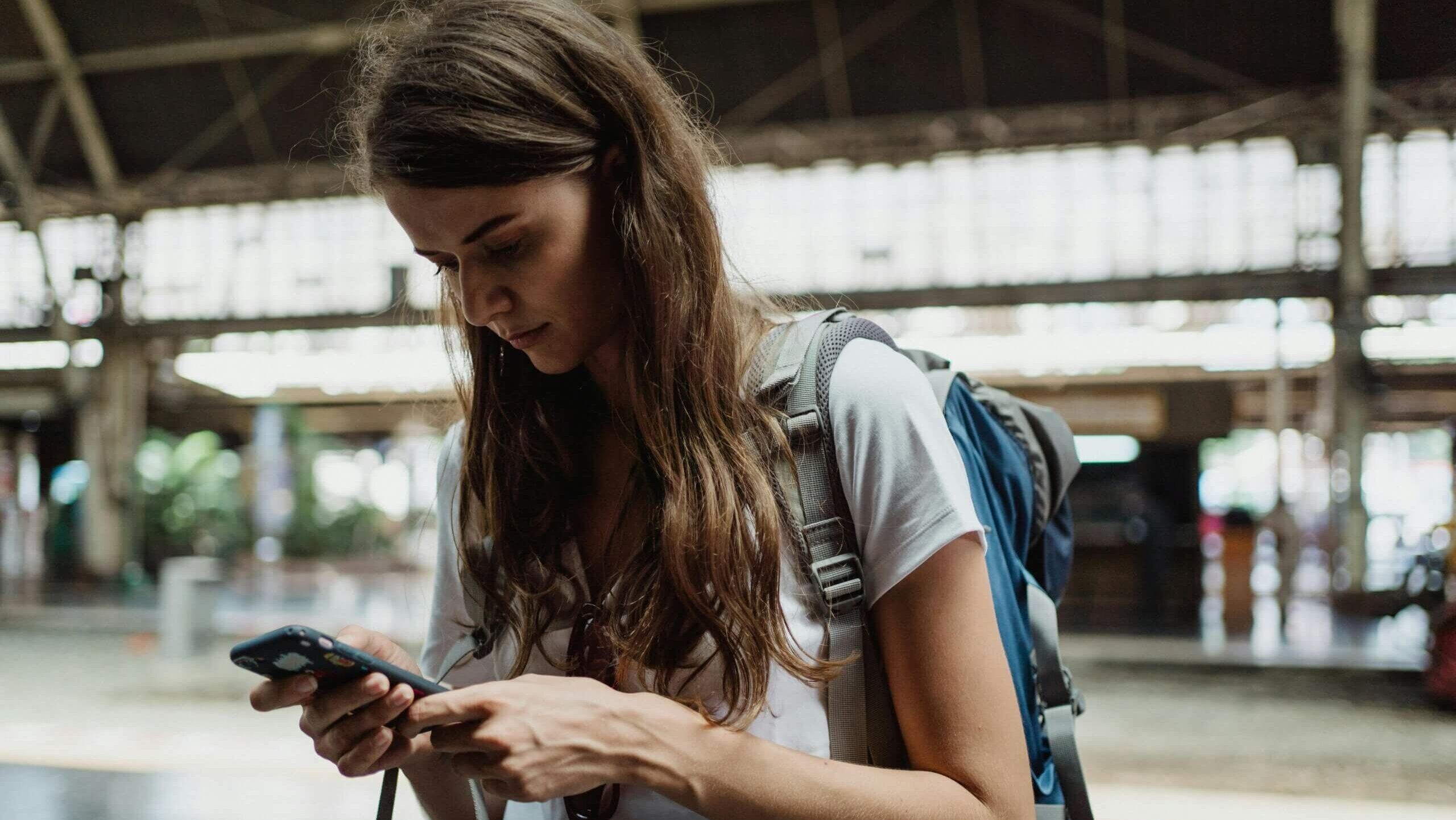 Wanita muda dengan ransel melihat smartphone di stasiun kereta.