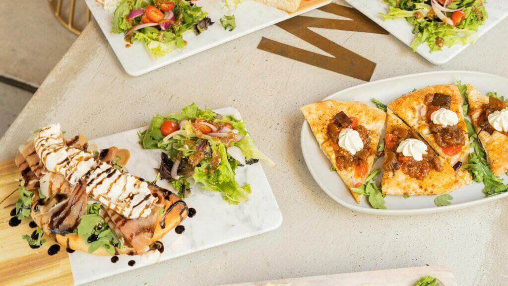 Salad dengan tomat ceri dan bawang bombay disajikan dengan roti pipih dengan topping krim dan chutney di atas piring marmer dan kayu.