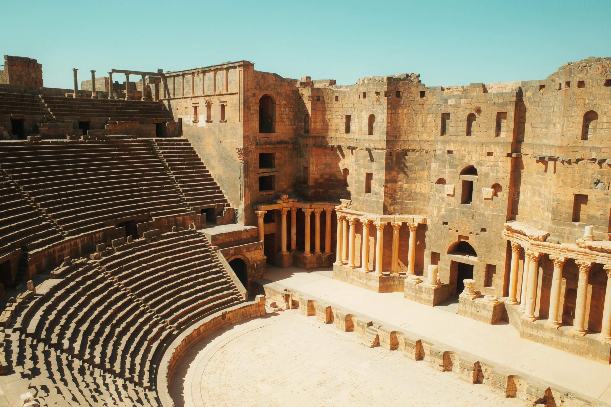 Reruntuhan teater Romawi kuno dengan tempat duduk batu berjenjang dan kolom di bawah langit biru cerah