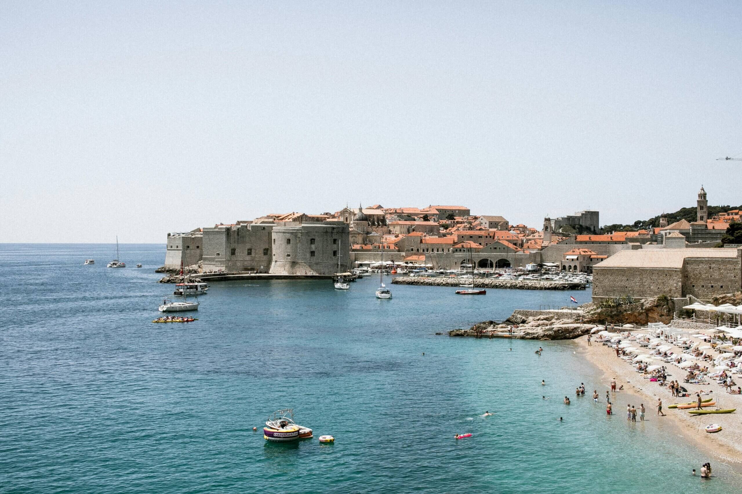 Pengunjung pantai berenang dan berjemur di dekat dinding batu bersejarah Dubrovnik, Kroasia dengan perahu di Laut Adriatik.