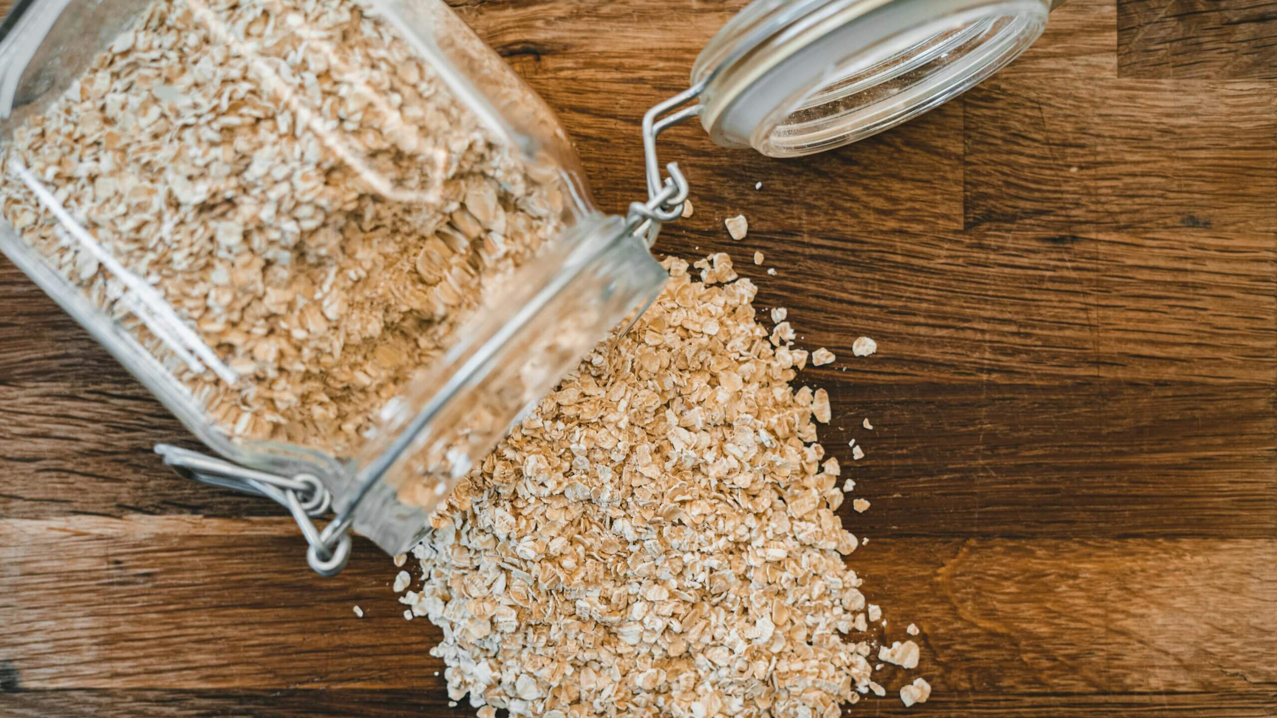 Toples kaca menumpahkan gandum gulung ke permukaan kayu