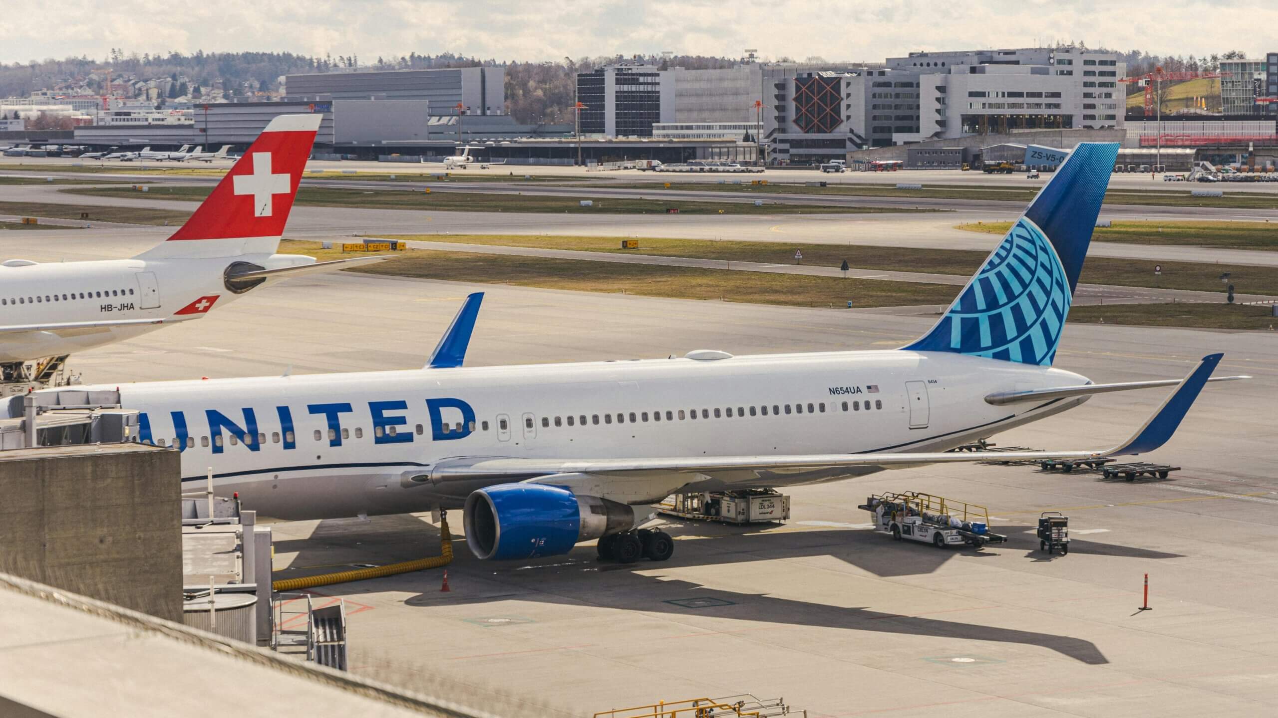 Pesawat United Airlines diparkir di gerbang bandara dengan ekor pesawat Swiss International Air Lines terlihat di dekatnya.