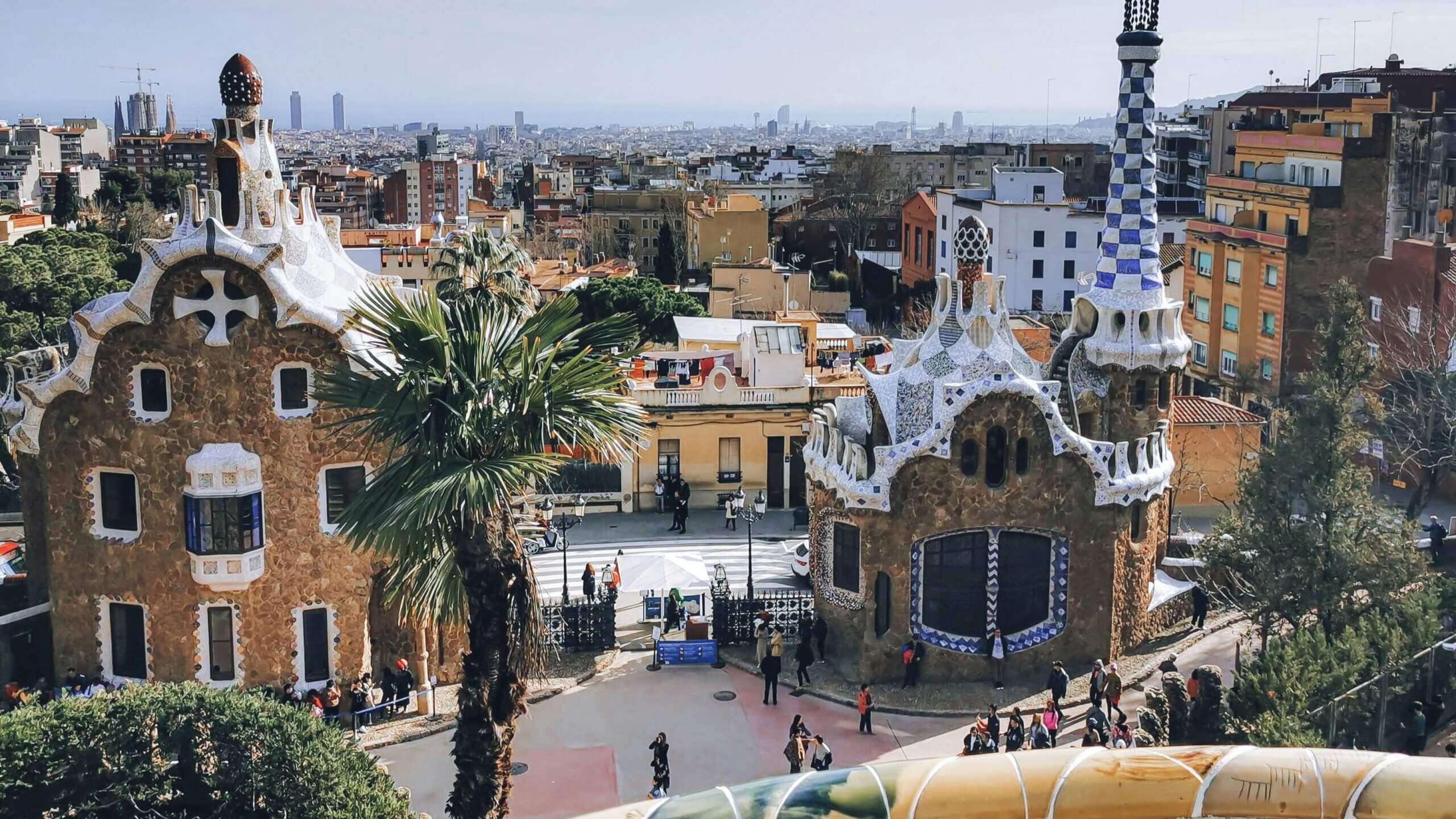 Bangunan ubin mosaik Gaudí dan pemandangan kota di Park Güell, Barcelona dengan pengunjung berjalan-jalan.