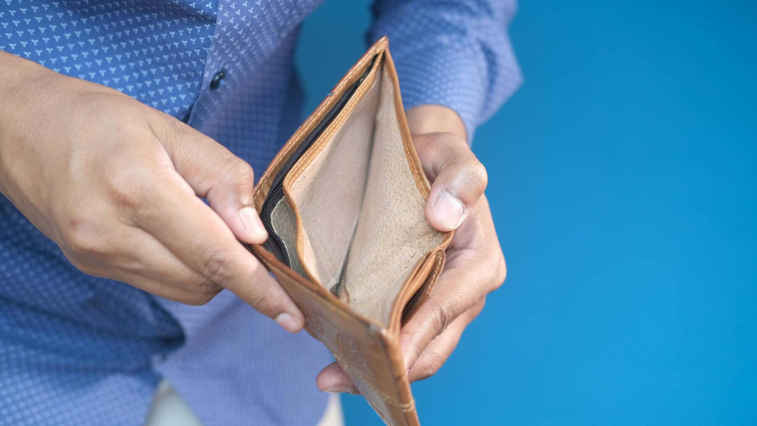 Orang yang memegang dompet kulit coklat kosong dengan latar belakang biru