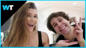 Two smiling young adults, one making a peace sign, in a bright indoor setting with a WT logo.