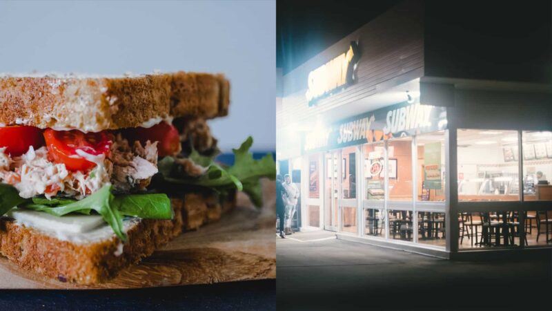 Tuna sandwich with lettuce and tomato next to a lit Subway restaurant at night with two people outside.