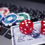 Red dice and poker chips on a credit card placed on a laptop keyboard representing online gambling.