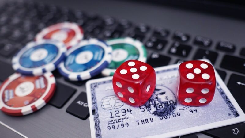 Red dice and poker chips on a credit card placed on a laptop keyboard representing online gambling.