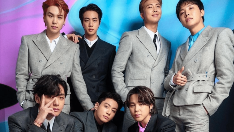 BTS members posing in stylish suits against a colorful blue and purple background.