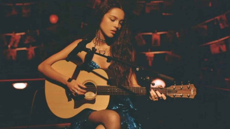 Woman playing acoustic guitar on stage with microphone in dimly lit setting