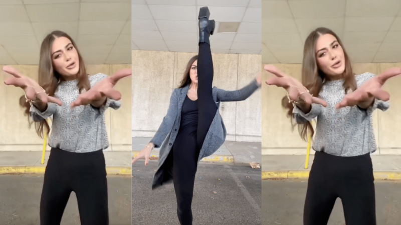 Woman in black pants and gray top performing a high kick and expressive hand gestures against a concrete wall background