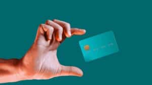 Hand holding a teal credit card with a chip against a teal background.