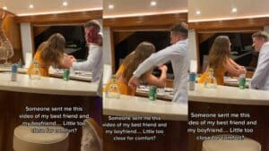 A woman in an orange dress and a man in a white shirt interact closely in a kitchen with drinks on the counter.