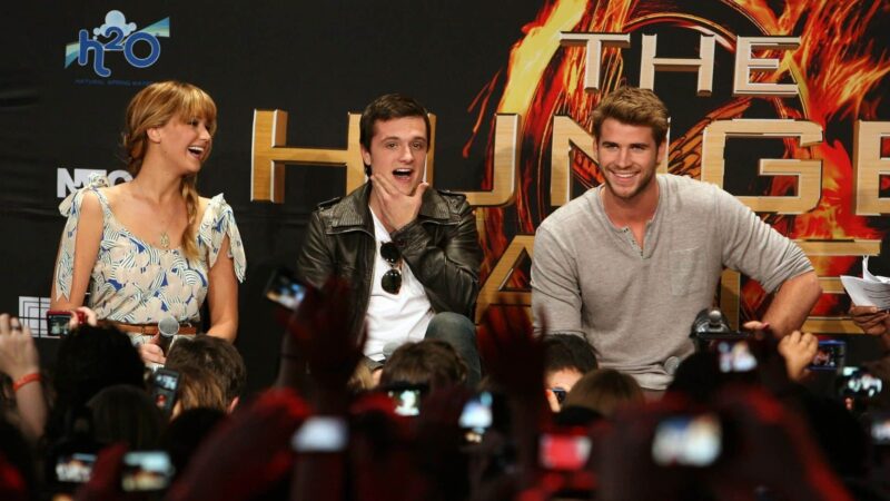 Jennifer Lawrence, Josh Hutcherson, and Liam Hemsworth at a The Hunger Games press event smiling and interacting with fans.