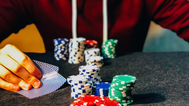 Person in red hoodie holding playing cards with stacks of poker chips on a table