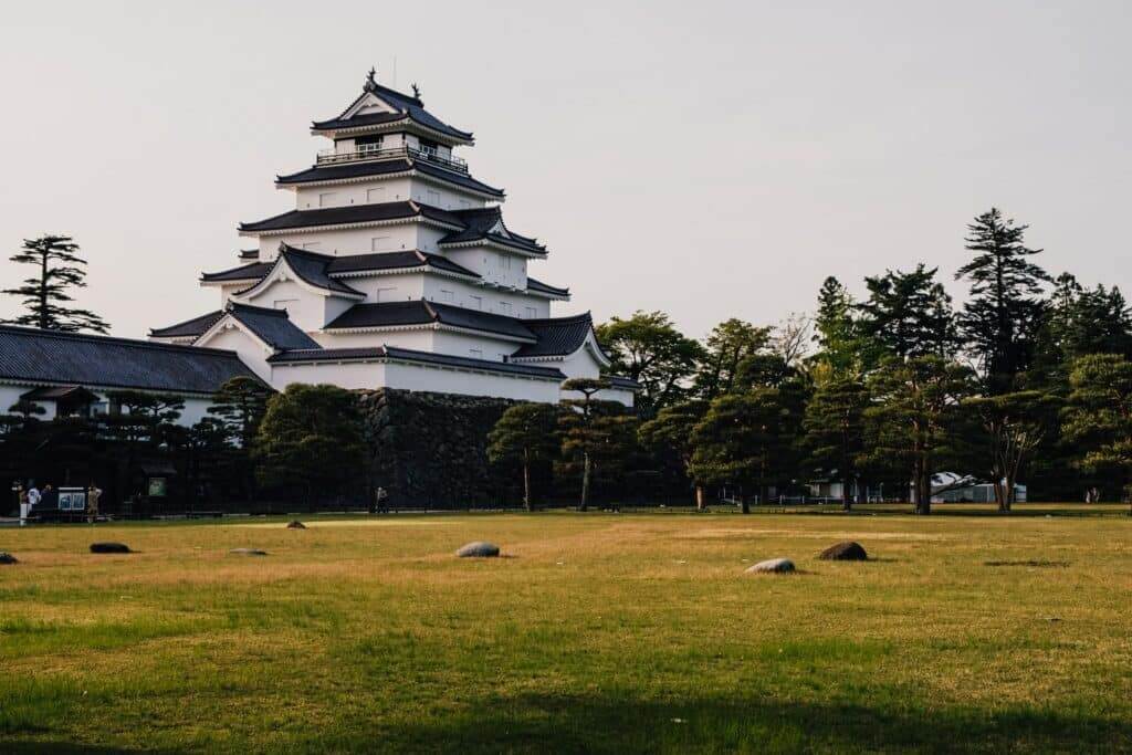 Tsuruga Castle, a traditional Japanese castle with white walls and black tiled roofs, surrounded by trees and grass.