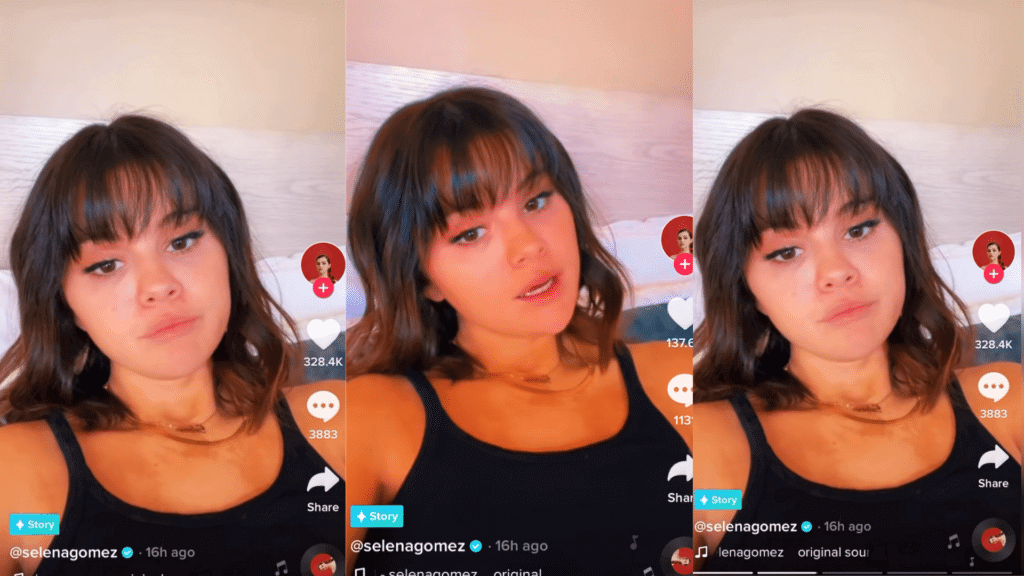 Selena Gomez in a black tank top recording a TikTok video lying on a bed with light wood headboard.