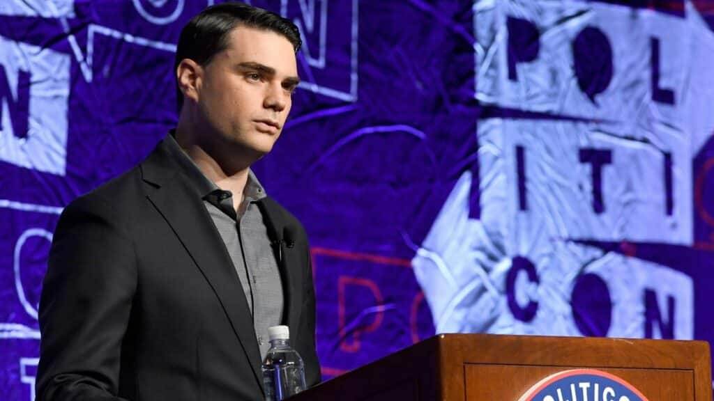 Ben Shapiro speaking at a Politicon event podium with a purple background banner.
