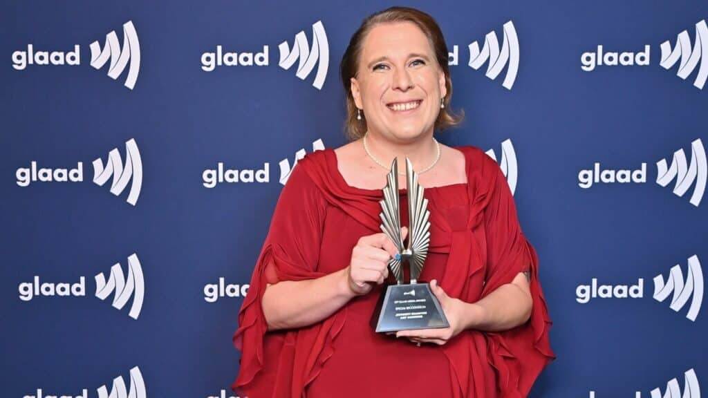 Person in red dress holding a GLAAD Media Award trophy against a blue GLAAD backdrop