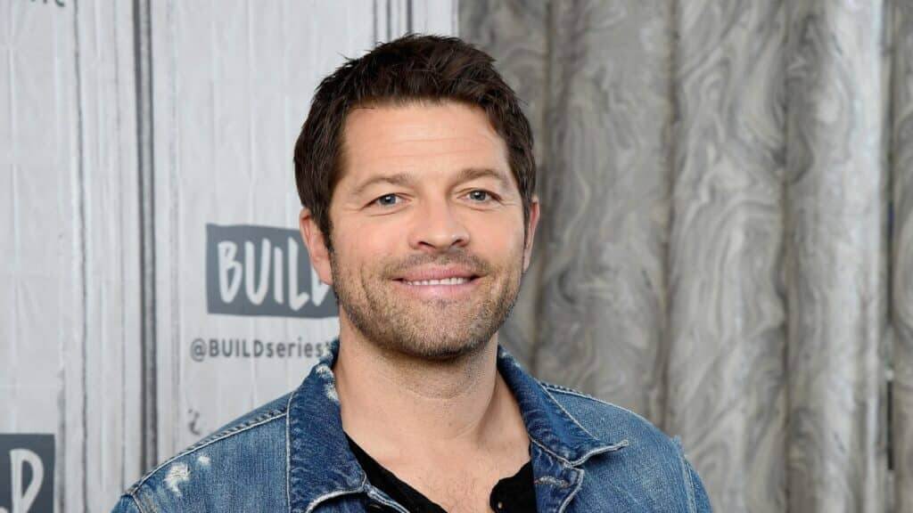 Misha Collins smiling in a denim jacket at a BUILD Series event.