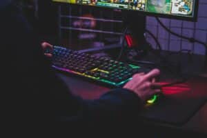 Person using a RGB backlit keyboard and gaming mouse while playing a video game on an ASUS monitor.