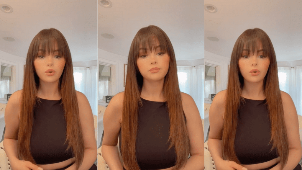 Selena Gomez with long straight hair and bangs wearing a black sleeveless top in a bright room